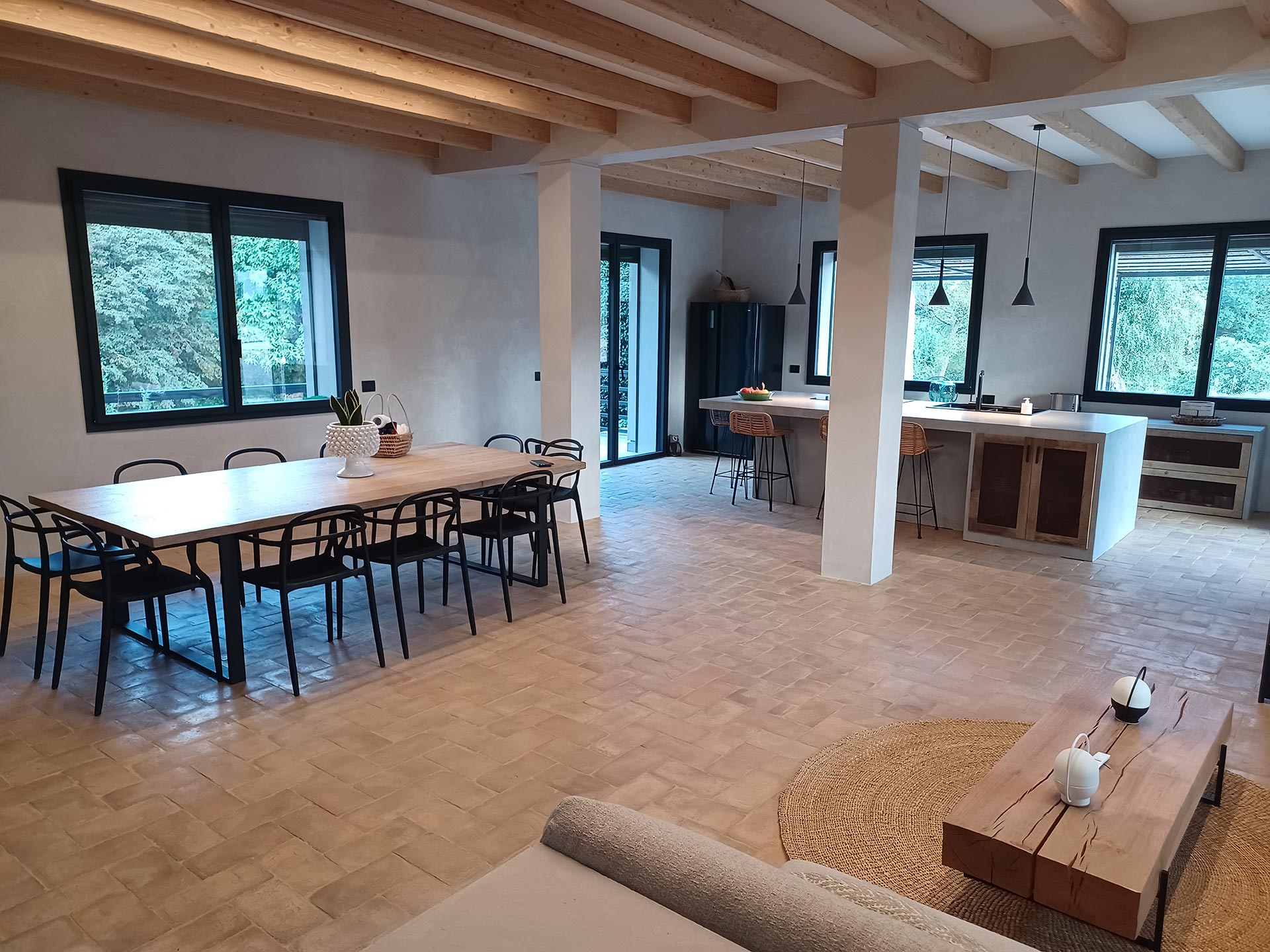 Open space cucine moderne con isola composto da una cucina con mobili in legno su misura e soggiorno con grande tavolo in legno di recupero al naturale e sedie in plexiglass nero.
