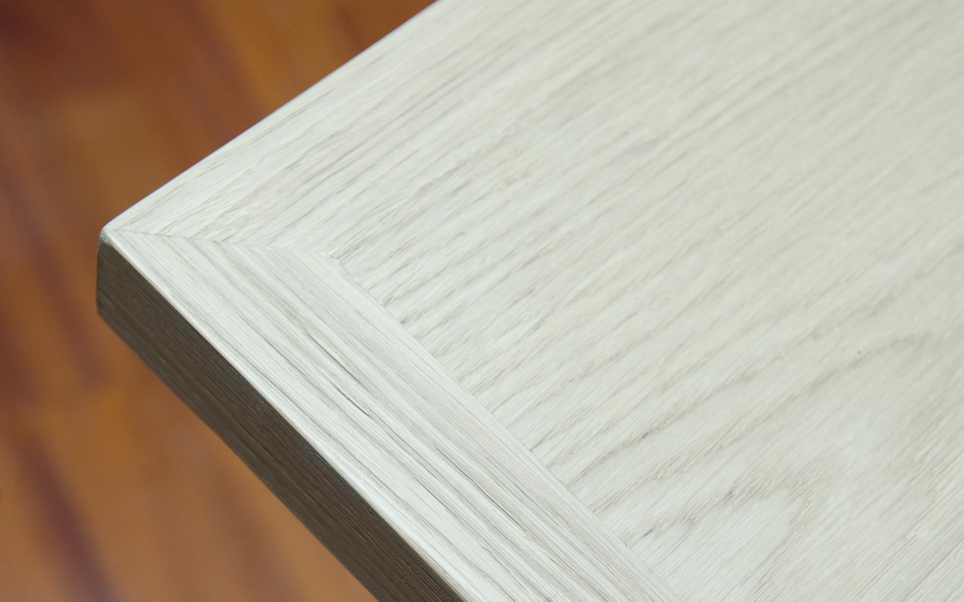 Primo piano di un tavolo artiginale in legno massello di rovere chiaro. Sullo sfondo parquet color miele.