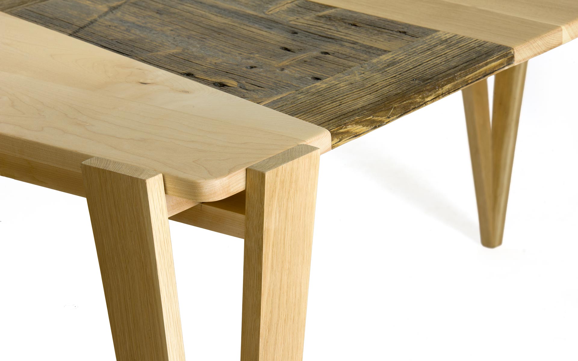 Dettaglio della gamba di uno dei tavoli in legno artigianali Laquercia21. In primo piano l'incontro di due pezzi di legno massello chiaro che si incastrano sotto al piano bicolore