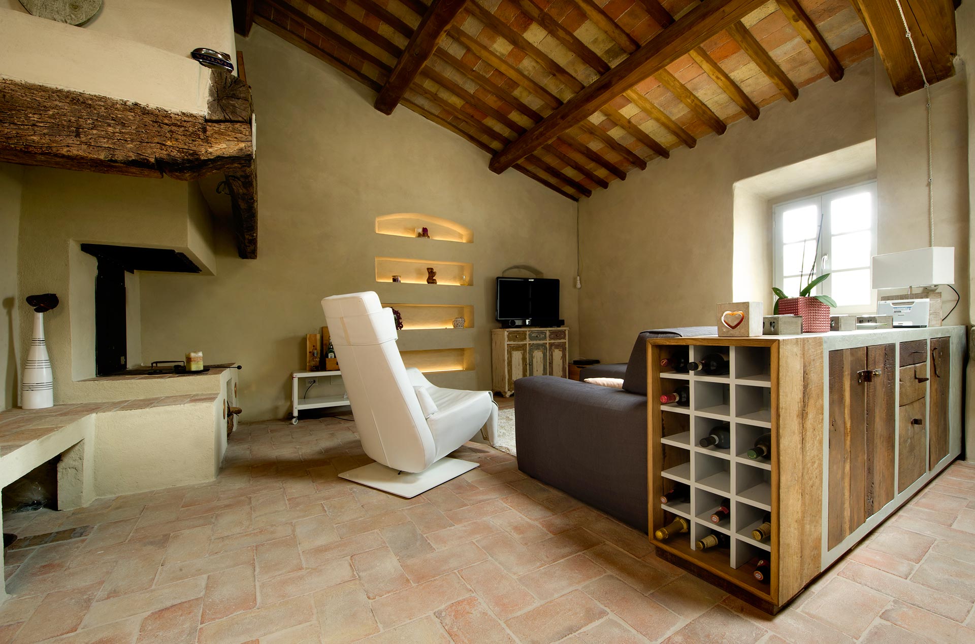 Vista totale di un open space in un casolare nel Chianti con soffitto a cassettoni in legno e mobili per soggiorno su misura in legno.